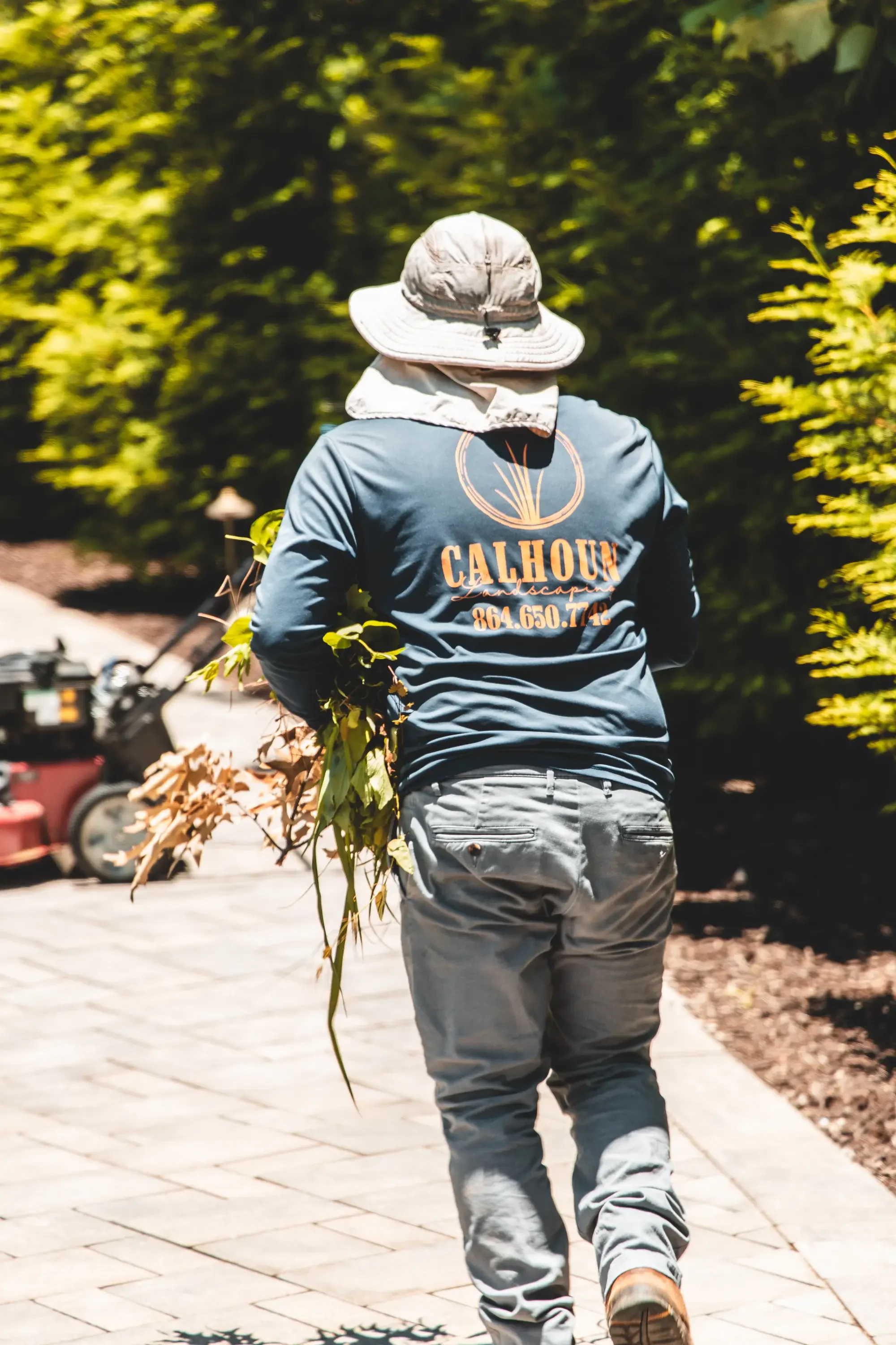Landscaper removing dead plant material from residential garden bed along paved pathway