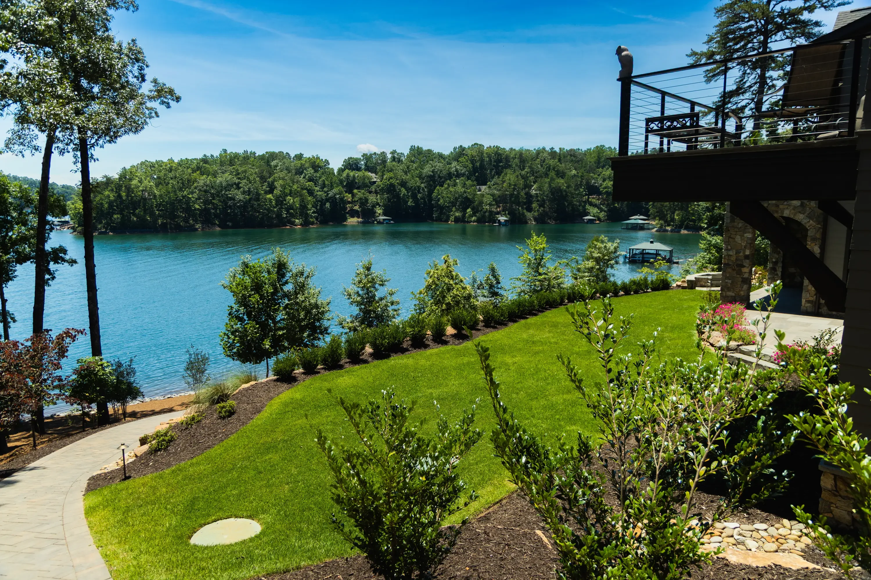 Waterfront landscape with manicured lawn, shrub plantings, and stone borders overlooking blue lake